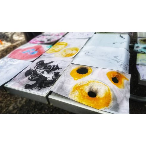 Drying marbled paper on a bench tabletop, striking yellow piece with black eyes